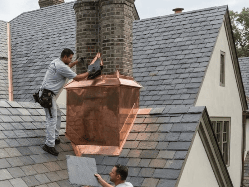 Roofer installing copper chimney flashing on a shingle roof, the masonry-to-roof joint that leaks first on prewar Lynbrook homes