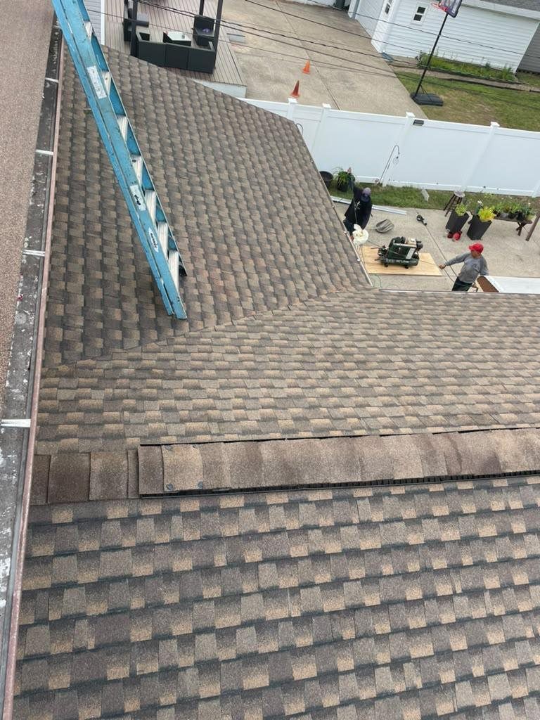 Bluemaster Roofing crew finishing a brown architectural shingle roof replacement with ridge vent on a Nassau County home near Lynbrook