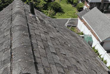 Wind-lifted ridge caps and an open porch-roof joint on a raised canal home in Oceanside, Nassau County, before repair